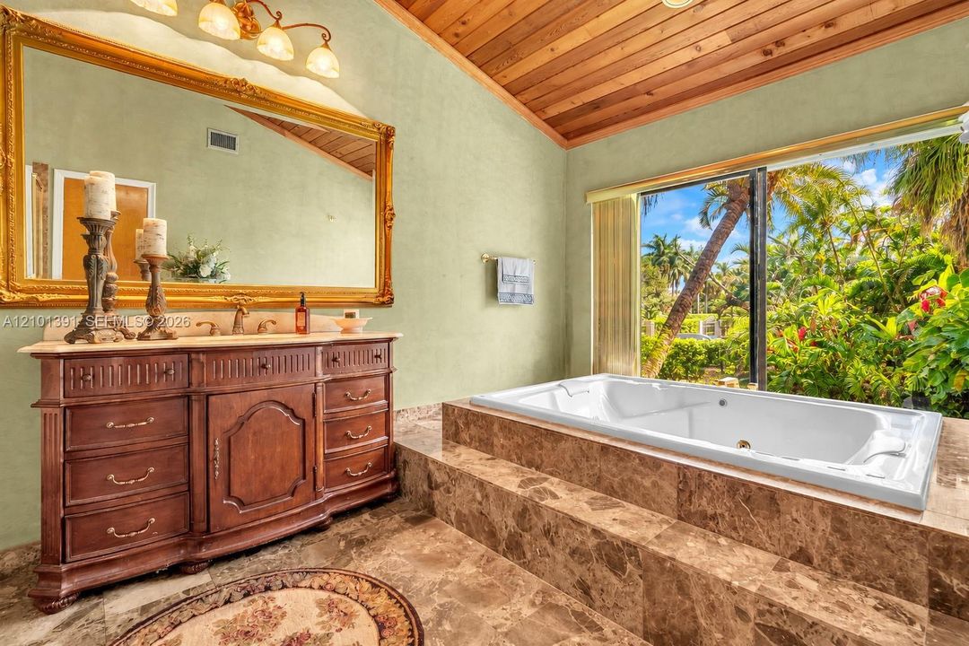 Soaking tub with surrounding stone tile, wood-paneled ceiling, and a decorative vanity with a rectangular sink