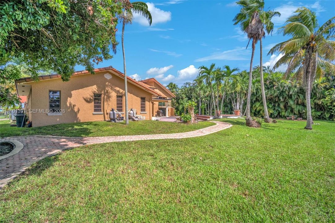 Expansive green lawn, mature palm trees, brick paver pathway, and an exterior with a stucco finish