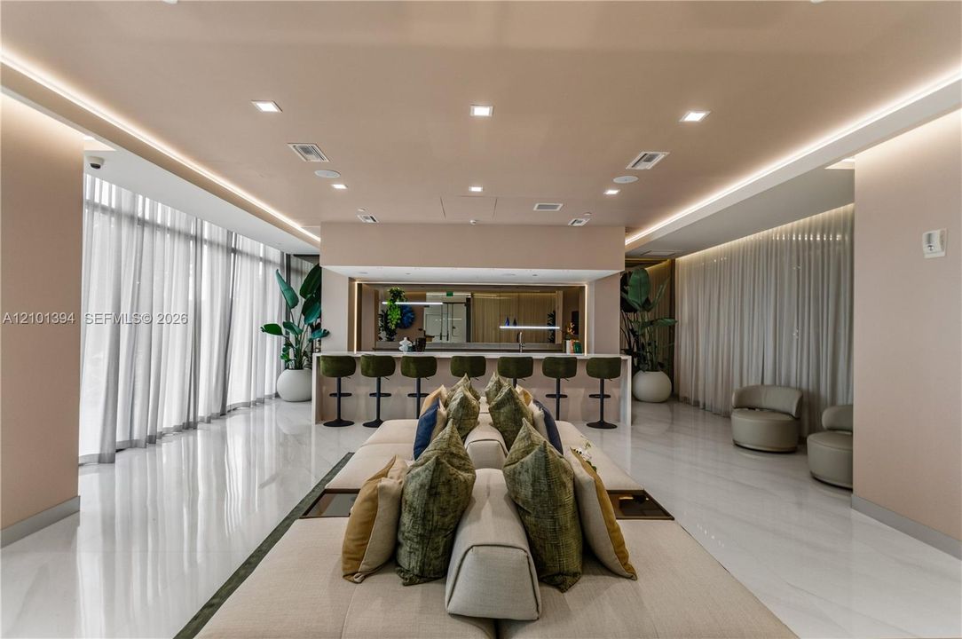 Open-concept space featuring polished stone-finish flooring, floor-to-ceiling sheer window treatments, recessed cove lighting, and a built-in counter with an integrated sink