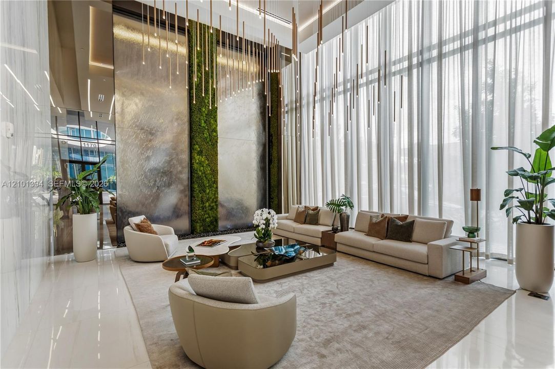 Double-height ceiling, floor-to-ceiling drapery, statement water feature with integrated moss panels, polished stone flooring, and multi-pendant contemporary lighting fixtures