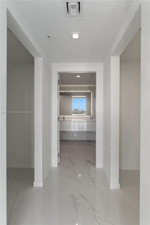Hallway featuring polished stone-finish tile flooring, recessed ceiling lighting, and crisp white trim