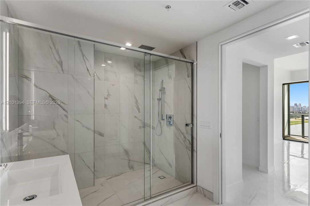 Walk-in shower featuring floor-to-ceiling stone-patterned tile, glass enclosure, and a chrome handheld shower fixture, paired with a white rectangular sink