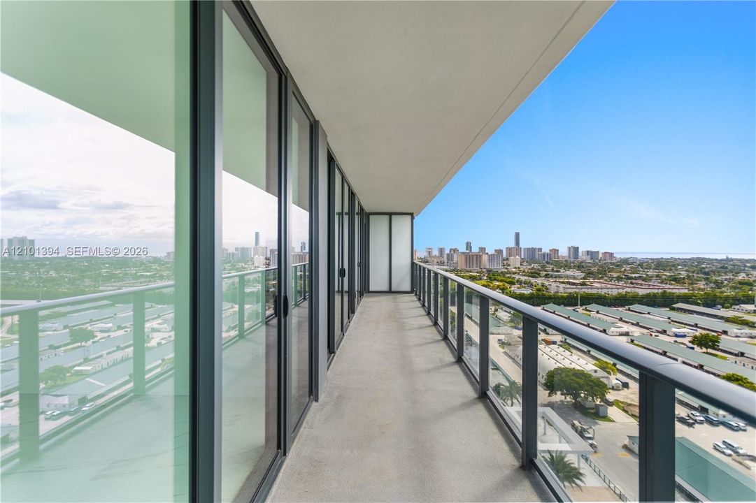 Covered balcony featuring full-height glass sliding doors, concrete flooring, and metal railings with glass panels