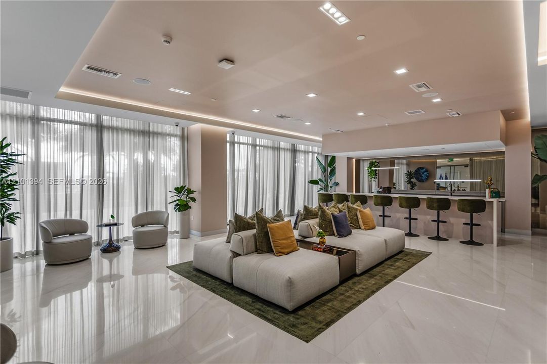 Large-format tile flooring, recessed LED ceiling lighting, floor-to-ceiling sheer window treatments, and a built-in counter with integrated bar seating
