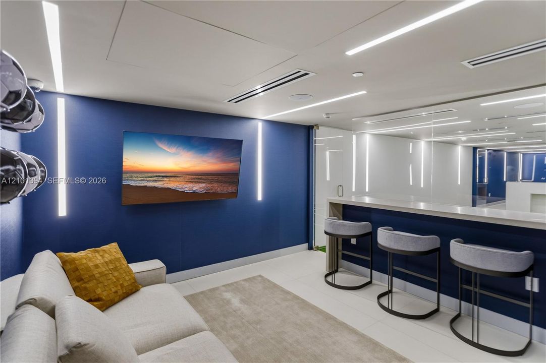 Custom interior featuring a built-in refreshment bar with a solid surface countertop, linear LED wall lighting, ceiling-recessed accent lights, and a full-height glass-paneled partition