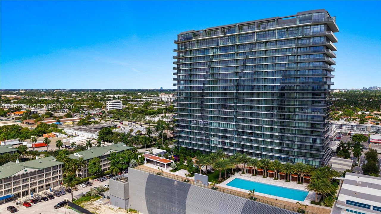 High-rise residential tower featuring glass-paneled balconies, a ground-level swimming pool, and landscaped outdoor surroundings