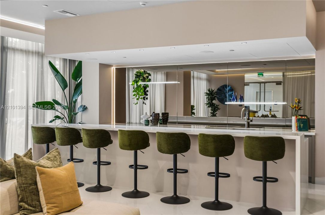 Oversized bar featuring a waterfall-edge stone countertop, expansive wall-to-wall mirror backsplash, integrated linear task lighting, and a single-basin undermount sink