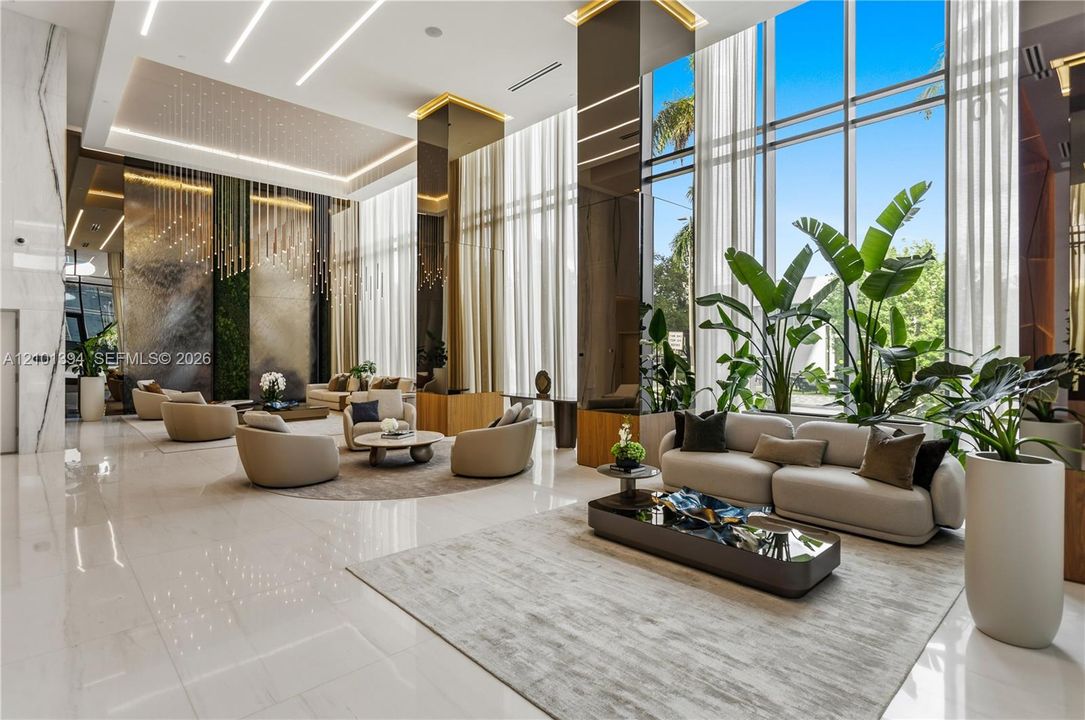 Grand lobby space featuring soaring floor-to-ceiling windows, polished stone flooring, custom vertical metallic wall paneling, and recessed linear LED ceiling lighting