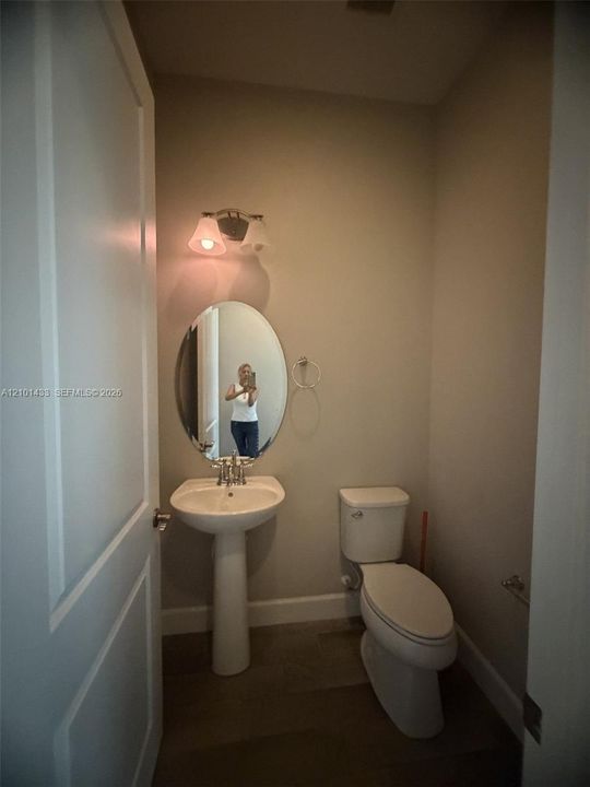 Pedestal sink, oval mirror, wall-mounted light fixture, and tile flooring