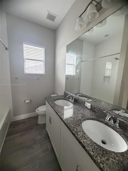Double vanity featuring stone-composite countertops, dual undermount sinks, wood-finish flooring, and a full-width vanity mirror with integrated multi-bulb lighting
