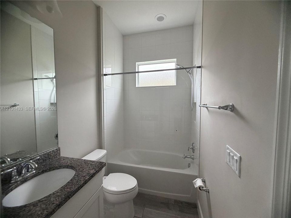 White tiled shower and tub with a privacy window, complemented by a vanity with a dark speckled countertop and an undermount sink