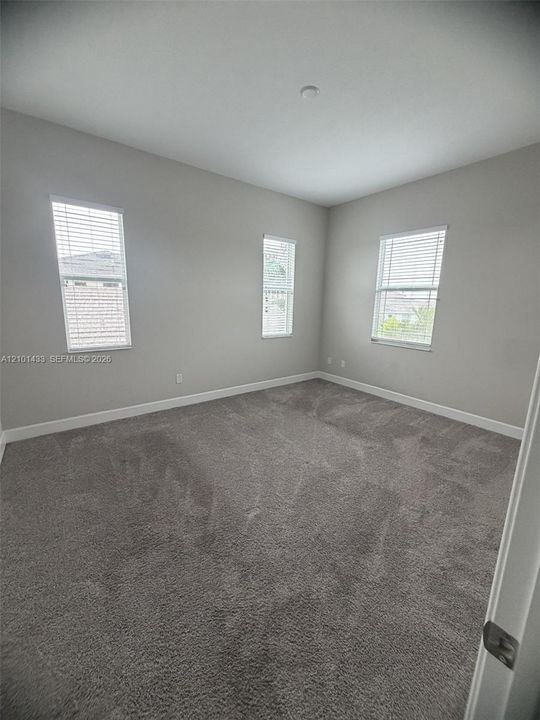 Neutral-toned interior room featuring wall-to-wall carpeting and three windows with fitted blinds