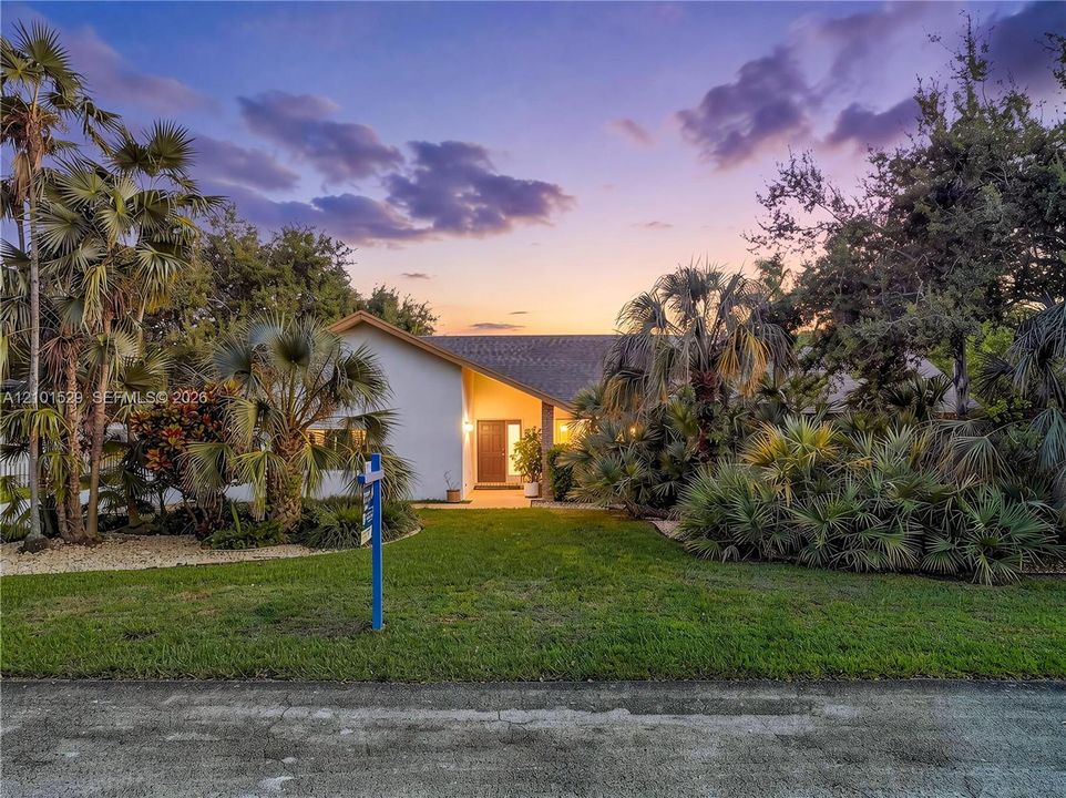 Pitched roofline, white exterior, mature palm trees, diverse landscaping, and a manicured lawn