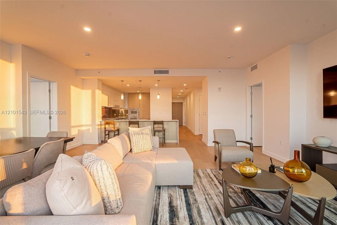 Open-concept living space featuring wood-finish flooring, recessed lighting, and a kitchen equipped with a stone-top island, built-in cabinetry, and multi-pendant lighting