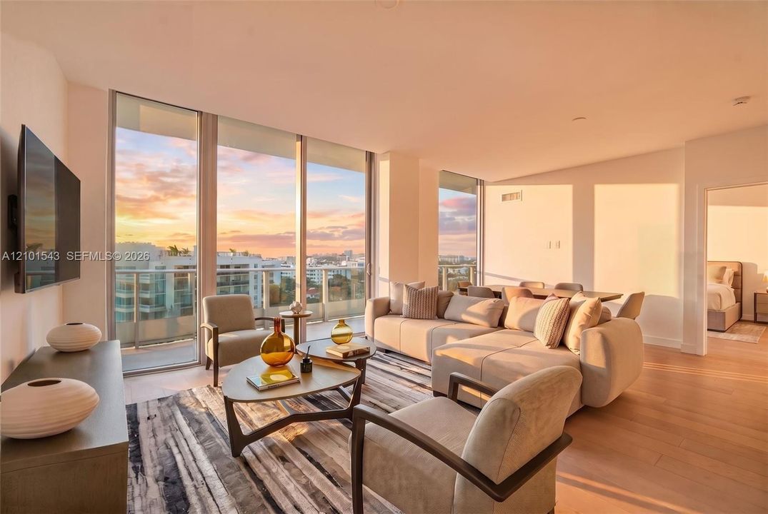 Floor-to-ceiling windows, wood-finish flooring, and a private balcony featuring a glass railing and expansive sky backdrop
