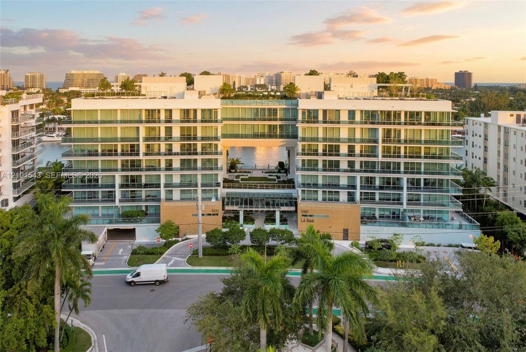 Mid-rise residential building featuring floor-to-ceiling glass paneling, wrap-around private balconies, and a central open-air atrium with ground-level landscaping