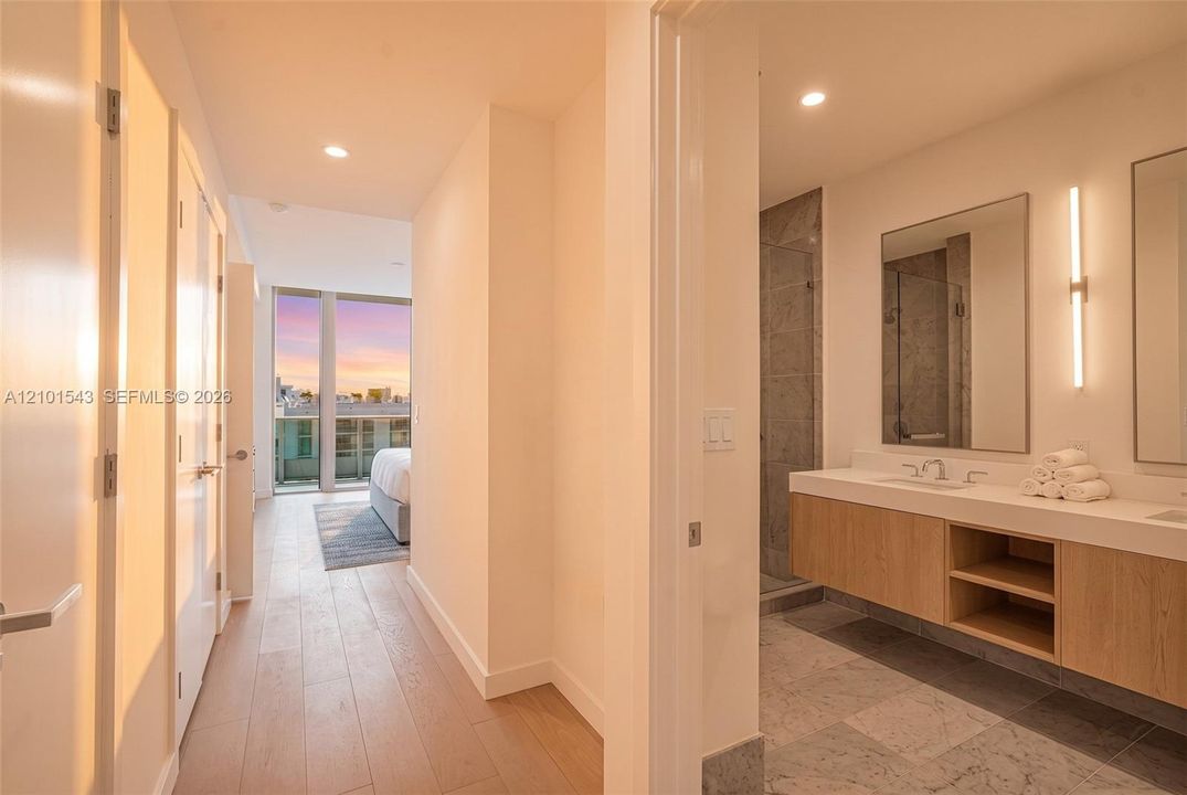 Floating wood-finish vanity with dual sinks, stone flooring, walk-in tile shower with glass enclosure, recessed lighting, and wall-mounted vanity mirrors