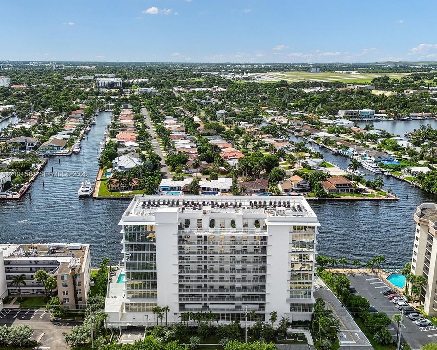 Aerial perspective of a multi-story building featuring floor-to-ceiling windows, private balconies, a flat roofline, and water frontage