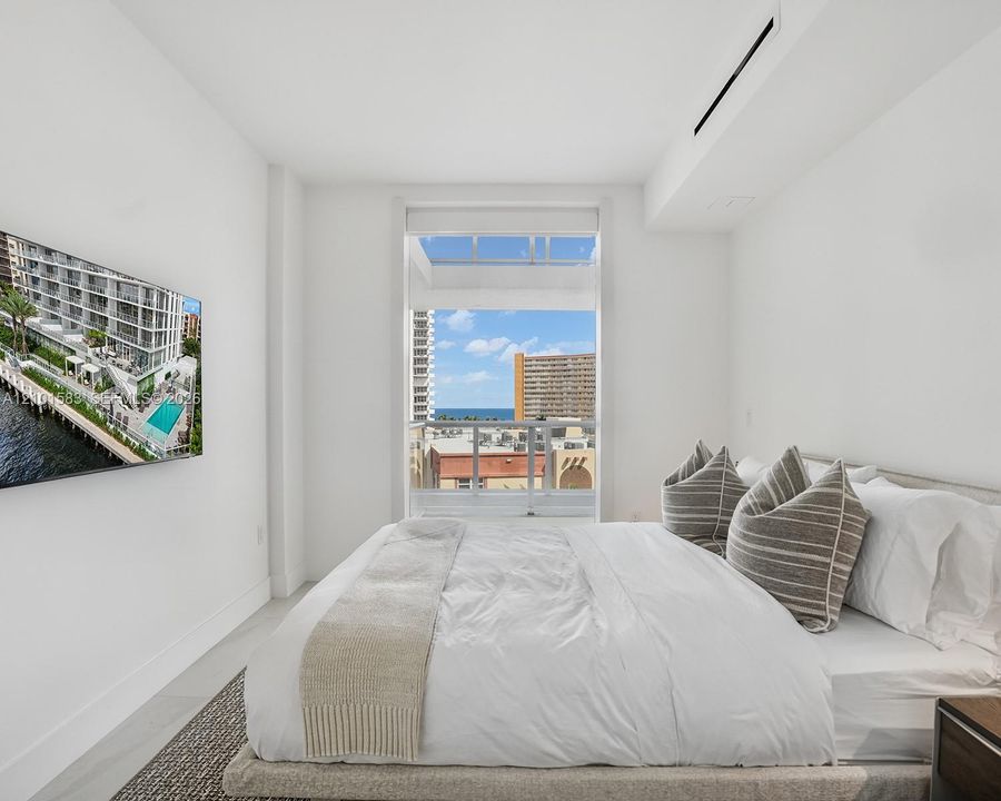 Floor-to-ceiling window featuring a glass balcony railing, neutral tile flooring, wall-mounted ductless climate control, and prominent water and cityscape scenery