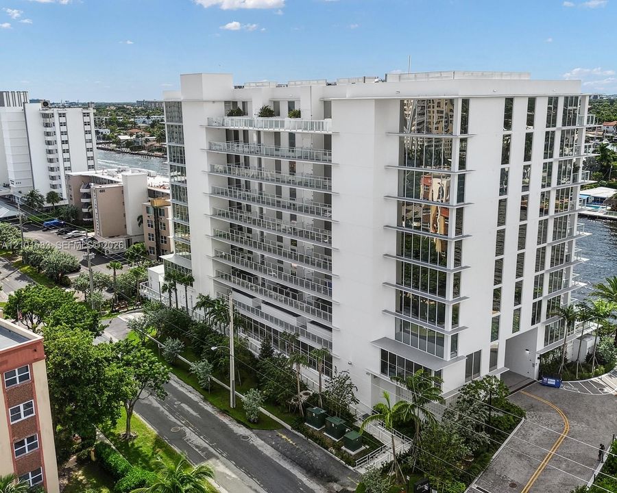 Mid-rise building featuring a white facade, extensive glass paneling, multiple levels of private balconies with railings, and waterfront positioning