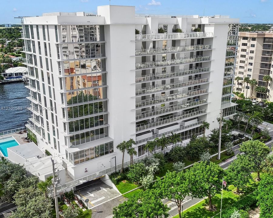 Multi-story residential building featuring floor-to-ceiling glass paneling, tiered cantilevered balconies with glass railings, an attached swimming pool, and dedicated subterranean parking access