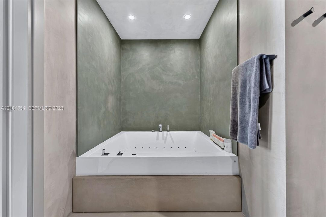 Primary bathroom with oversized spa tub and microcement walls.