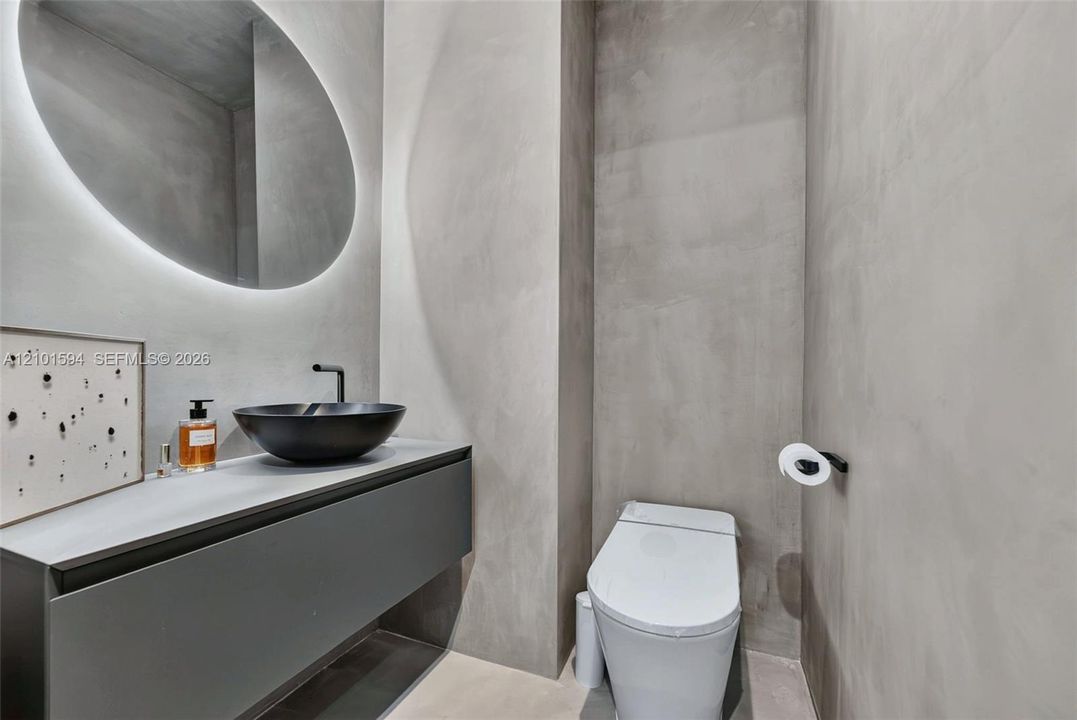 Powder room with floating vanity, vessel sink and round backlit mirror.