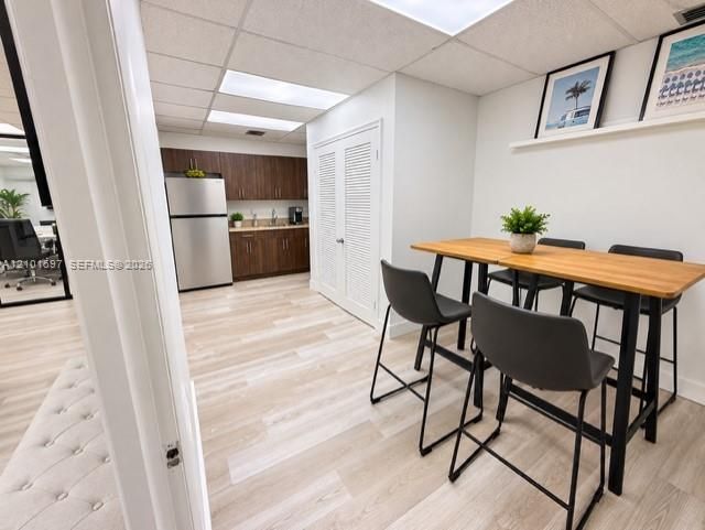Kitchenette featuring wood-finish cabinetry, stainless steel refrigerator, drop ceiling with recessed lighting, and wood-finish flooring