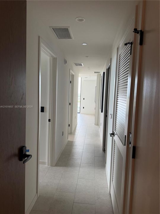 Hallway featuring large-format ceramic tile flooring, recessed ceiling lighting, and matte black hardware on solid-core wood doors, including a louvered closet door