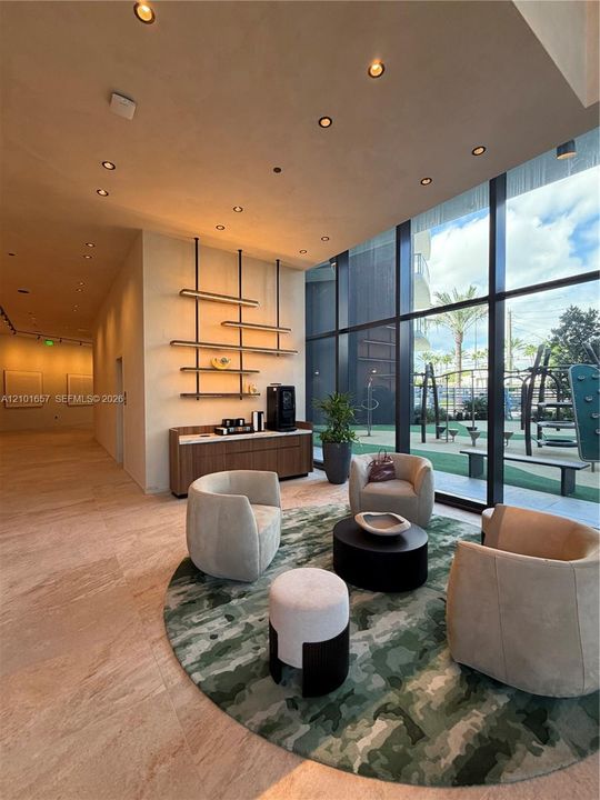 Floor-to-ceiling glass windows, recessed ceiling lighting, natural stone flooring, custom wall-mounted metal shelving, and a built-in wood-finish credenza with a stone countertop