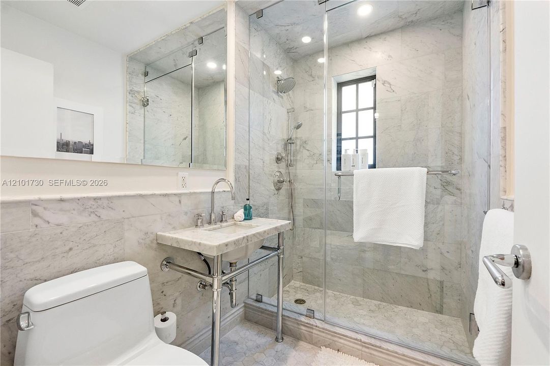 Bathroom featuring stone wall and floor tile, glass-enclosed shower with a handheld fixture, metal console sink, and a wall-to-wall mirror