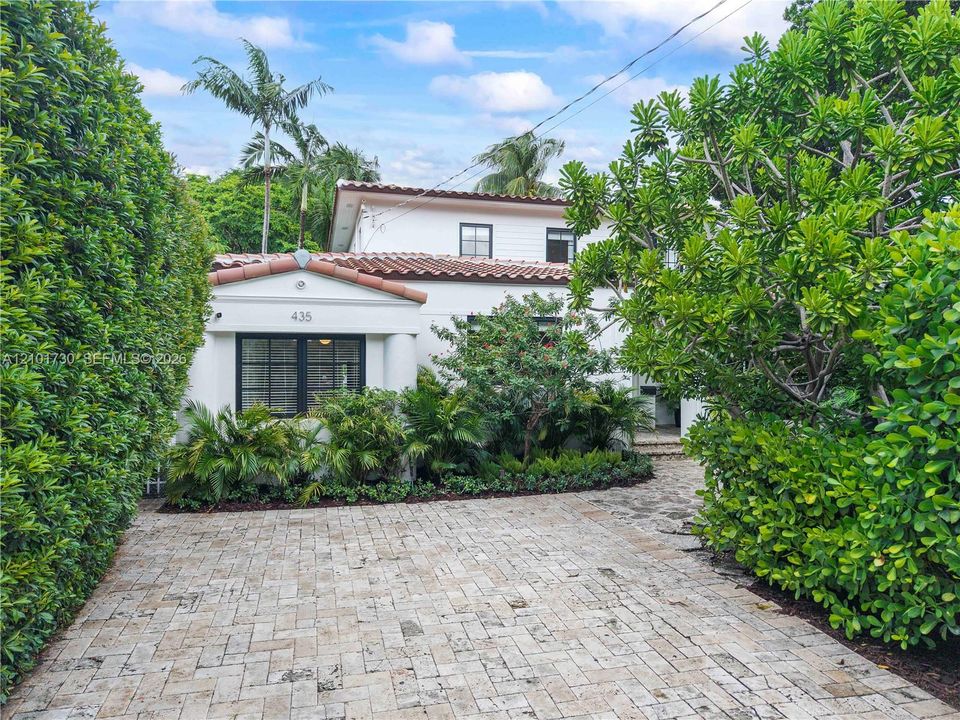 Exterior facade featuring a white stucco finish, decorative tile roof, multi-pane dark-framed windows, and a paved stone driveway