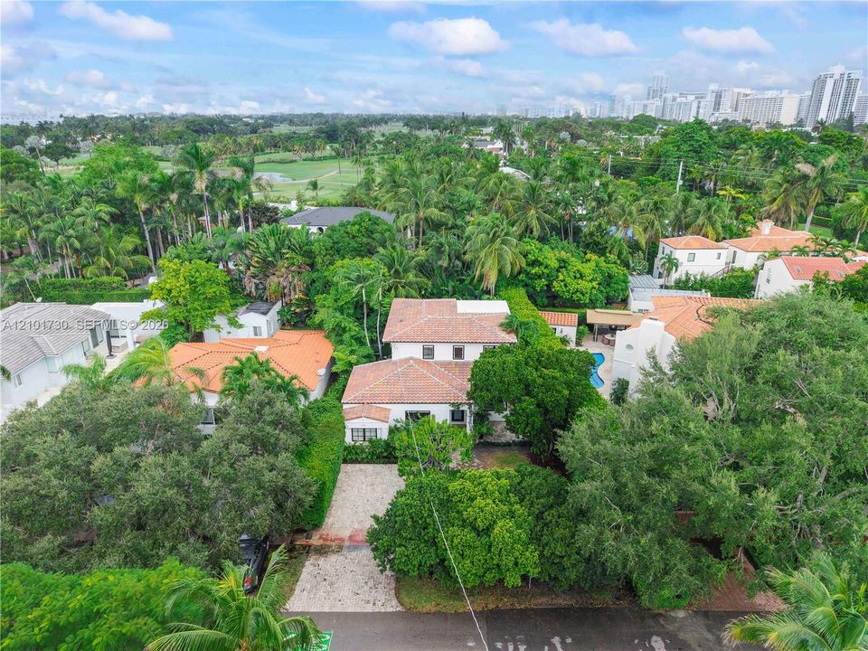 Multi-level residence featuring a clay tile roof, light-toned exterior finish, paver driveway, and mature landscaping