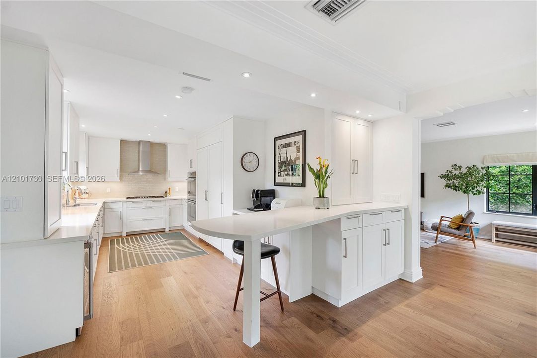 Kitchen featuring white shaker-style cabinetry, quartz countertops, integrated peninsula, stainless steel range hood, and wood-finish flooring