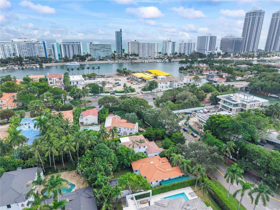 Aerial perspective of a coastal residential area featuring tile roofing, mature tropical foliage, private swimming pools, and proximity to the waterfront