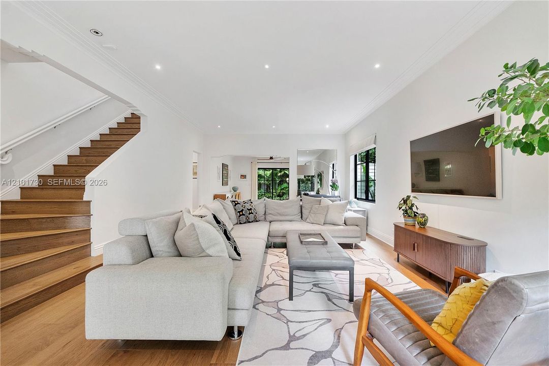 Living area featuring wood-finish flooring, staircase with wood treads, recessed lighting, crown molding, and large window with dark frame