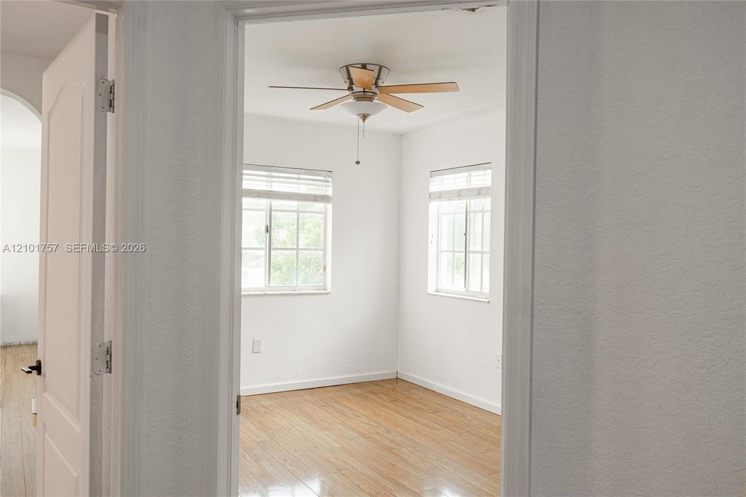 Wood-finish flooring with a ceiling fan light fixture and two windows with blinds