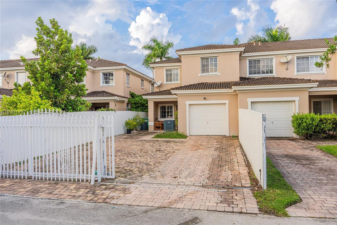 Two-story stucco exterior with white grid windows, barrel tile roof, and a private entry gate
