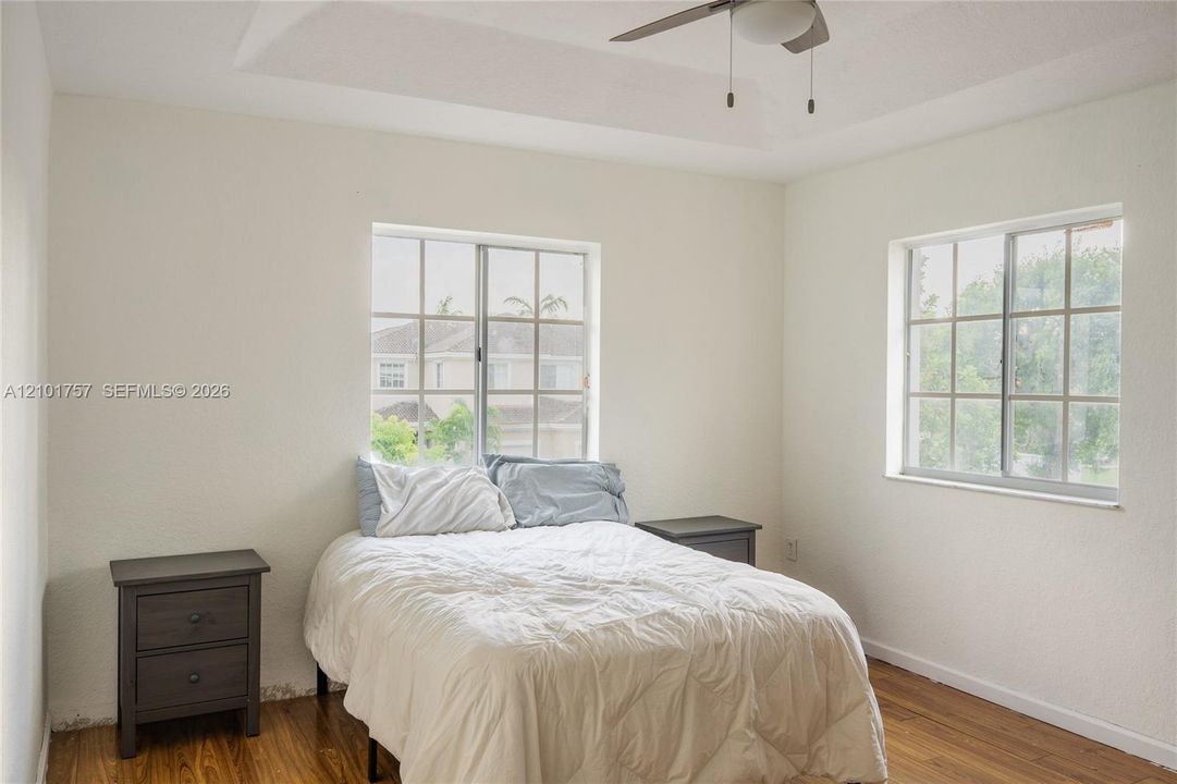 Tray ceiling with a ceiling fan light fixture, wood-finish flooring, and multiple windows