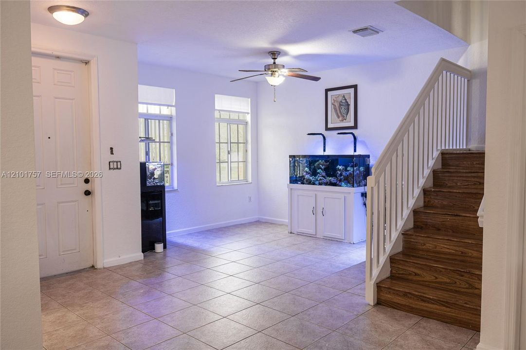Tiled flooring throughout, white paneled entry door, wood-finish staircase, ceiling fan light fixture, and multiple windows