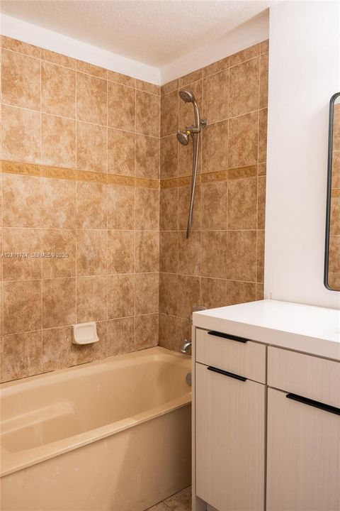 Bathtub with full-height tile surround, wall-mounted shower fixture, and a vanity with a light-toned countertop