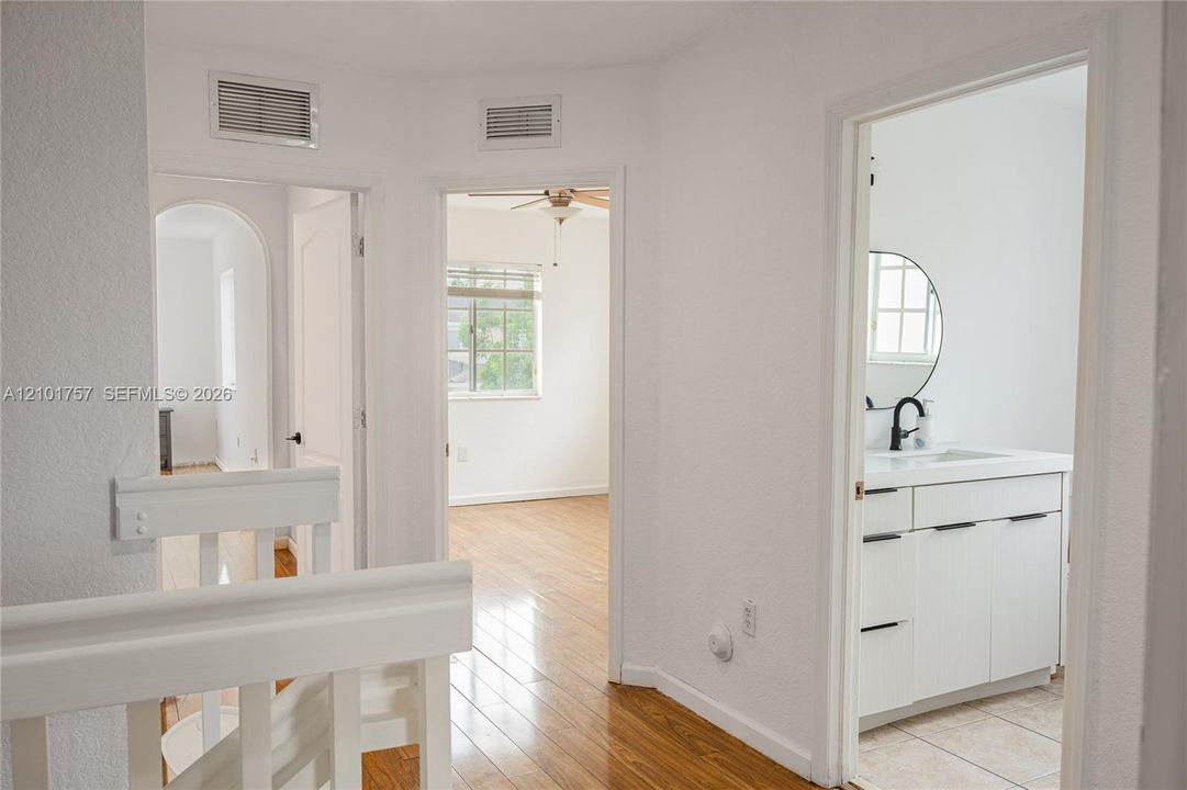 Hardwood-finish flooring, white painted walls, white spindle railings, white vanity with black hardware, and a round black-framed mirror