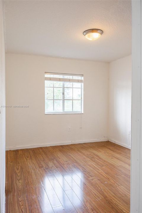 Wood-finish flooring with a window featuring horizontal blinds and a flush mount ceiling light