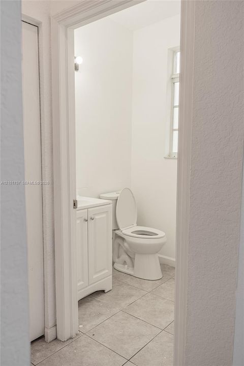 White vanity with dual cabinet doors, light-toned tile flooring, and a window