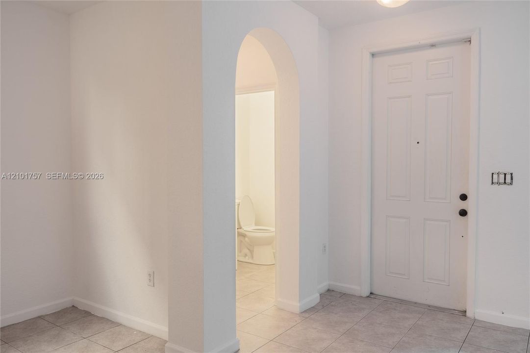 White paneled door, arched doorway, and light-toned tile flooring