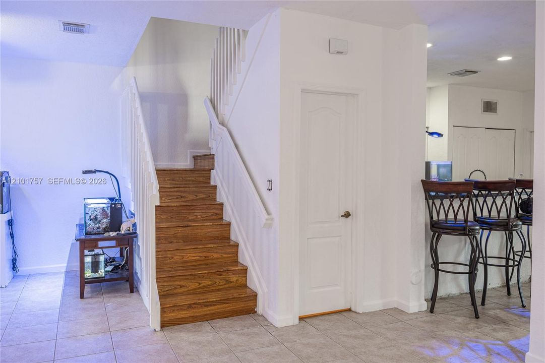 Wood-finish staircase with white risers and railing, white paneled door, and neutral-toned tile flooring