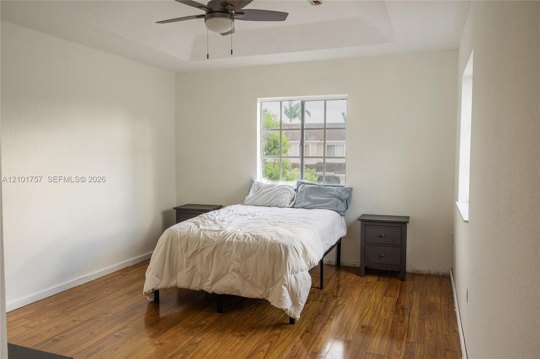 Tray ceiling with a ceiling fan, wood-finish flooring, and a large window