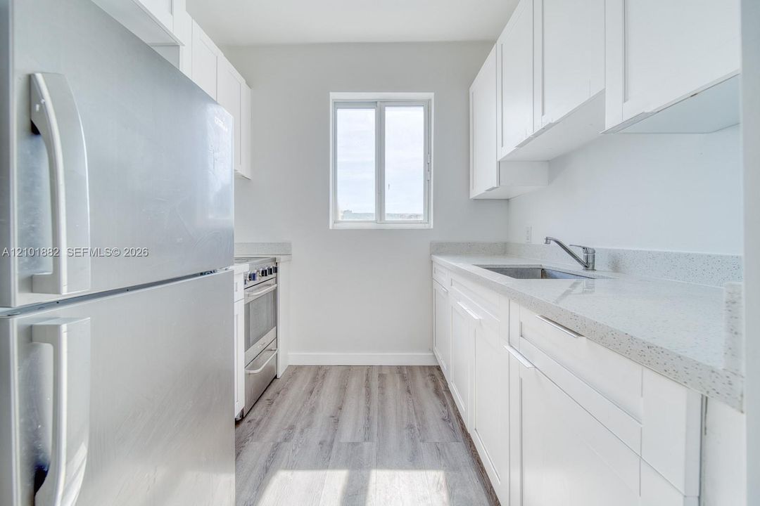Kitchen featuring white cabinetry, solid-surface countertops, stainless steel refrigerator and range, and wood-finish flooring