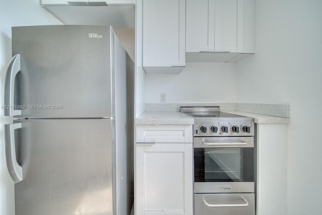 Kitchen featuring white shaker-style cabinetry, speckled stone-finish countertops, and stainless steel appliances including a refrigerator and a slide-in range