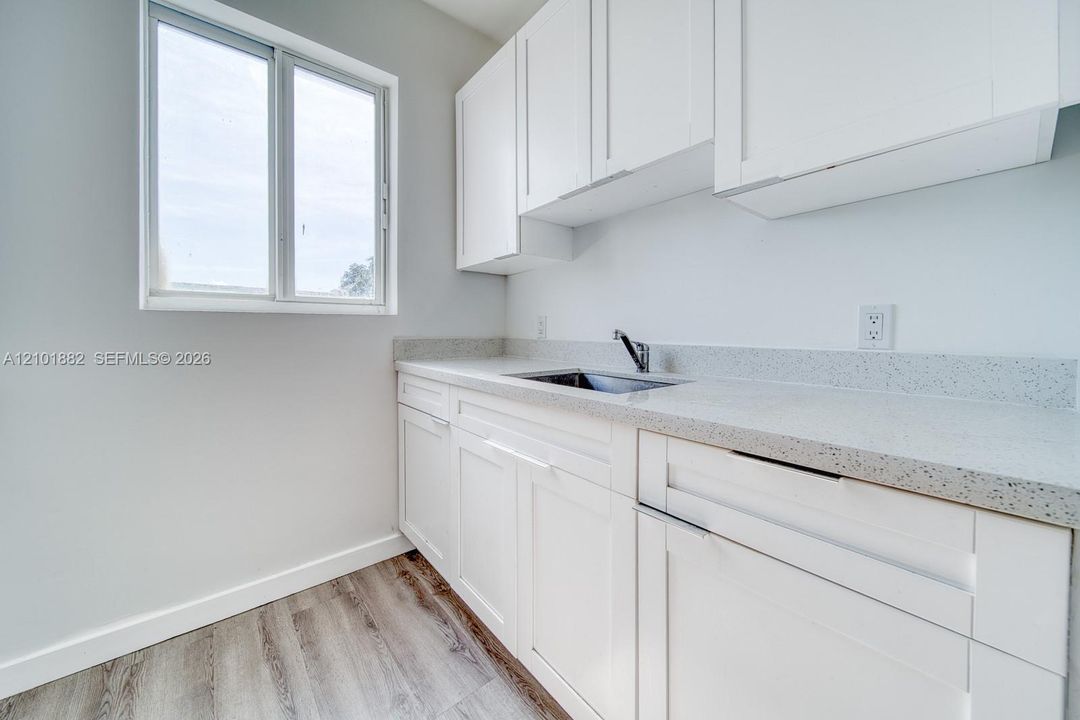 White shaker-style cabinetry, speckled stone-composite countertop, stainless steel undermount sink, gooseneck faucet, and wood-finish flooring